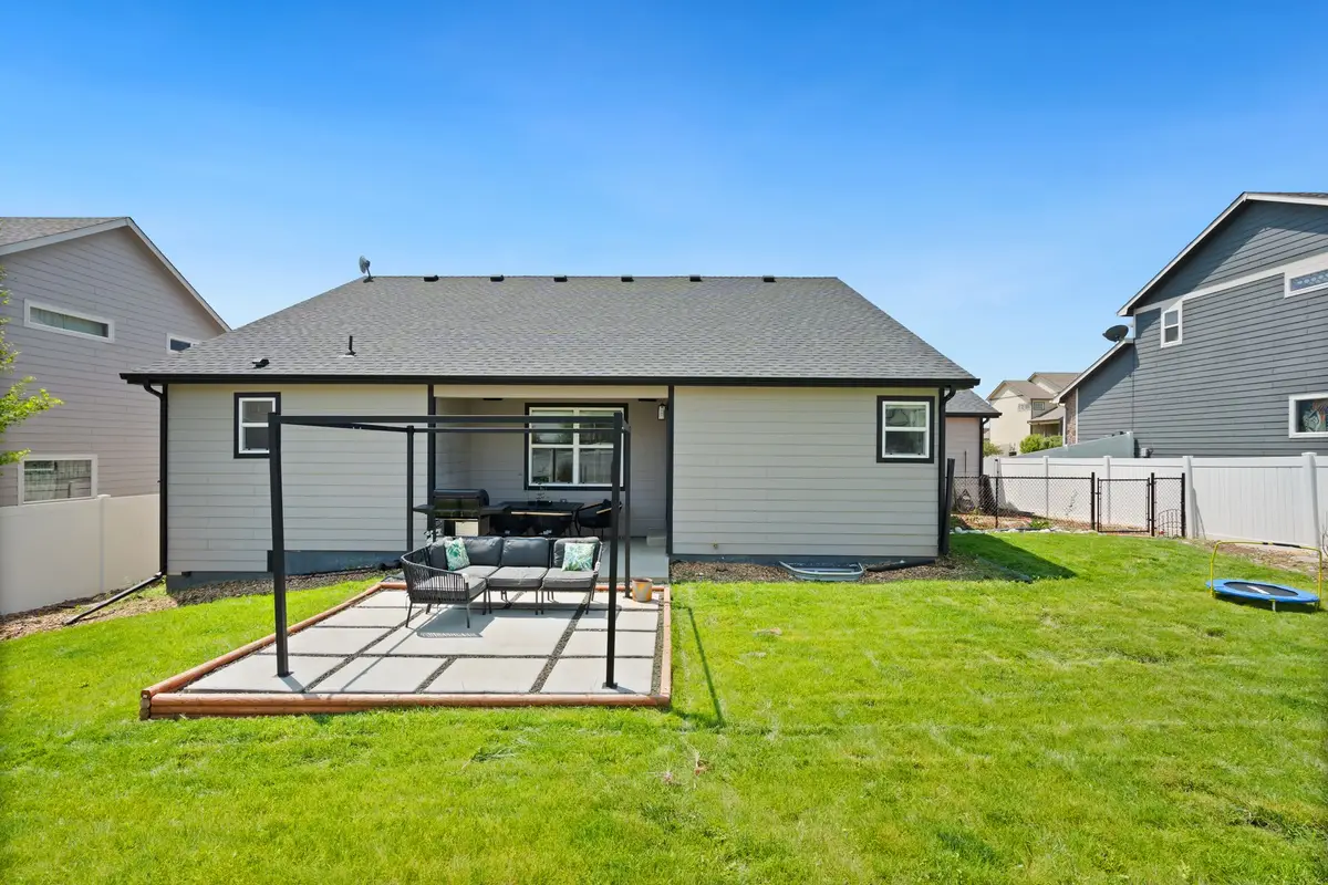 Backyard with a new paver patio, pergola and freshly mowed lawn behind a single-story home